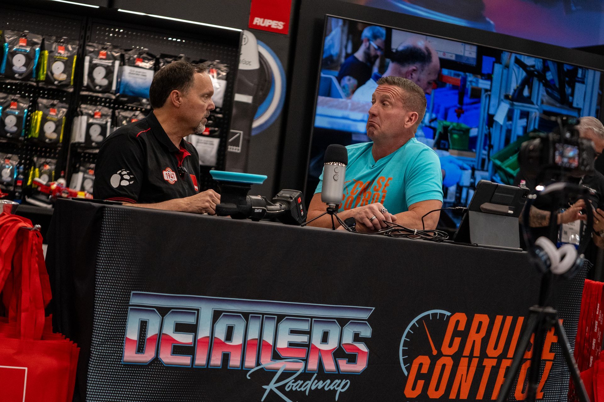 Two men are sitting at a table in a store talking to each other.
