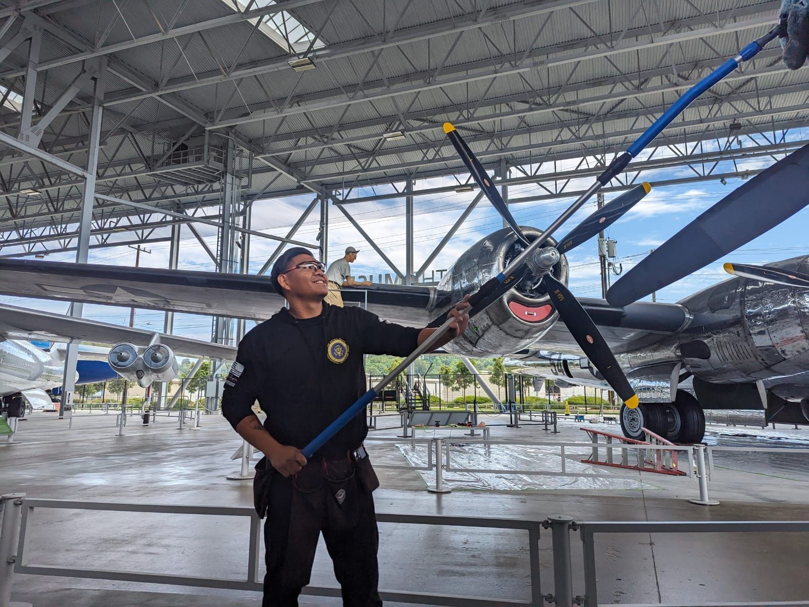A man is standing in front of an airplane in a hangar holding a broom.