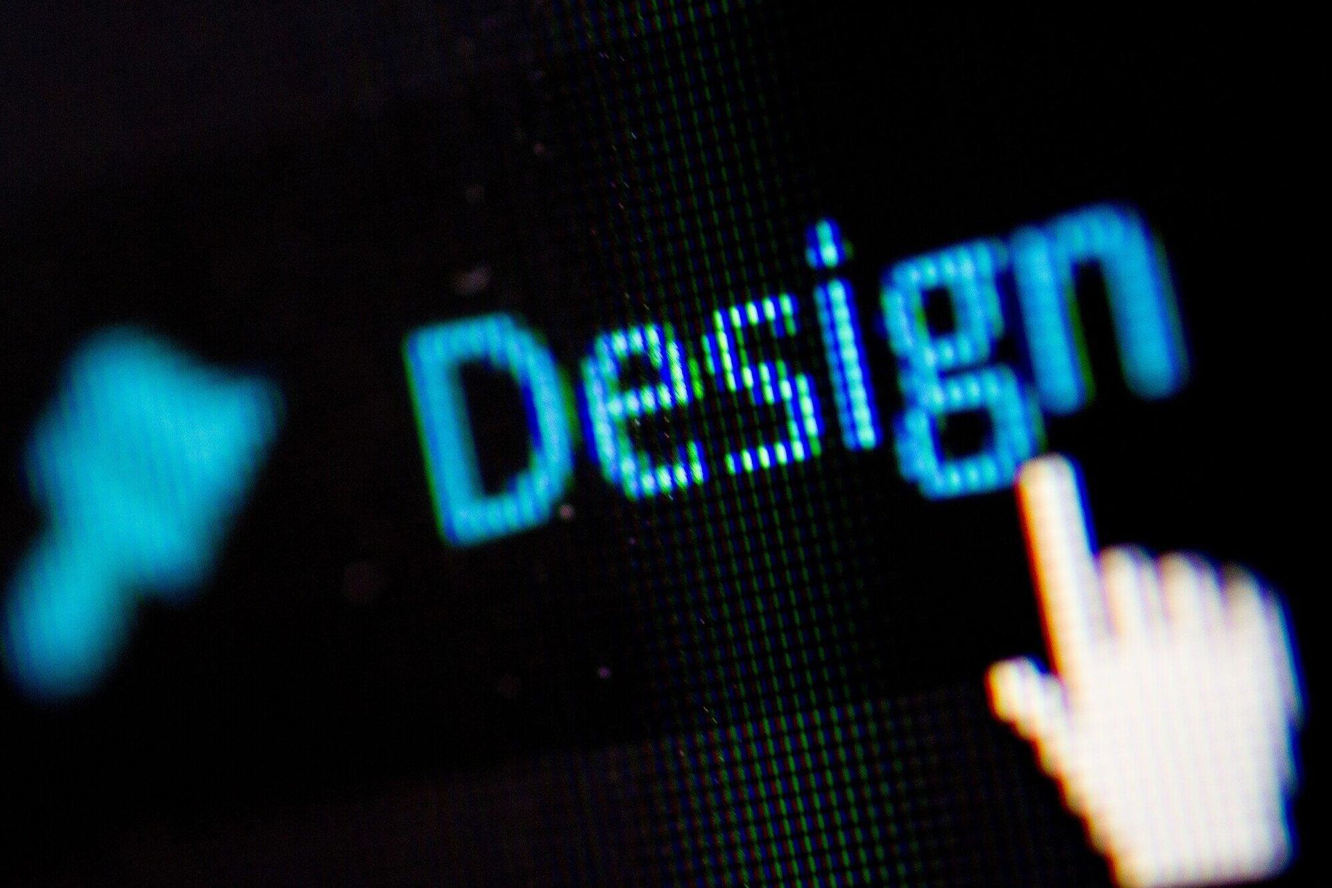 A hand is pointing at the word design on a computer screen.