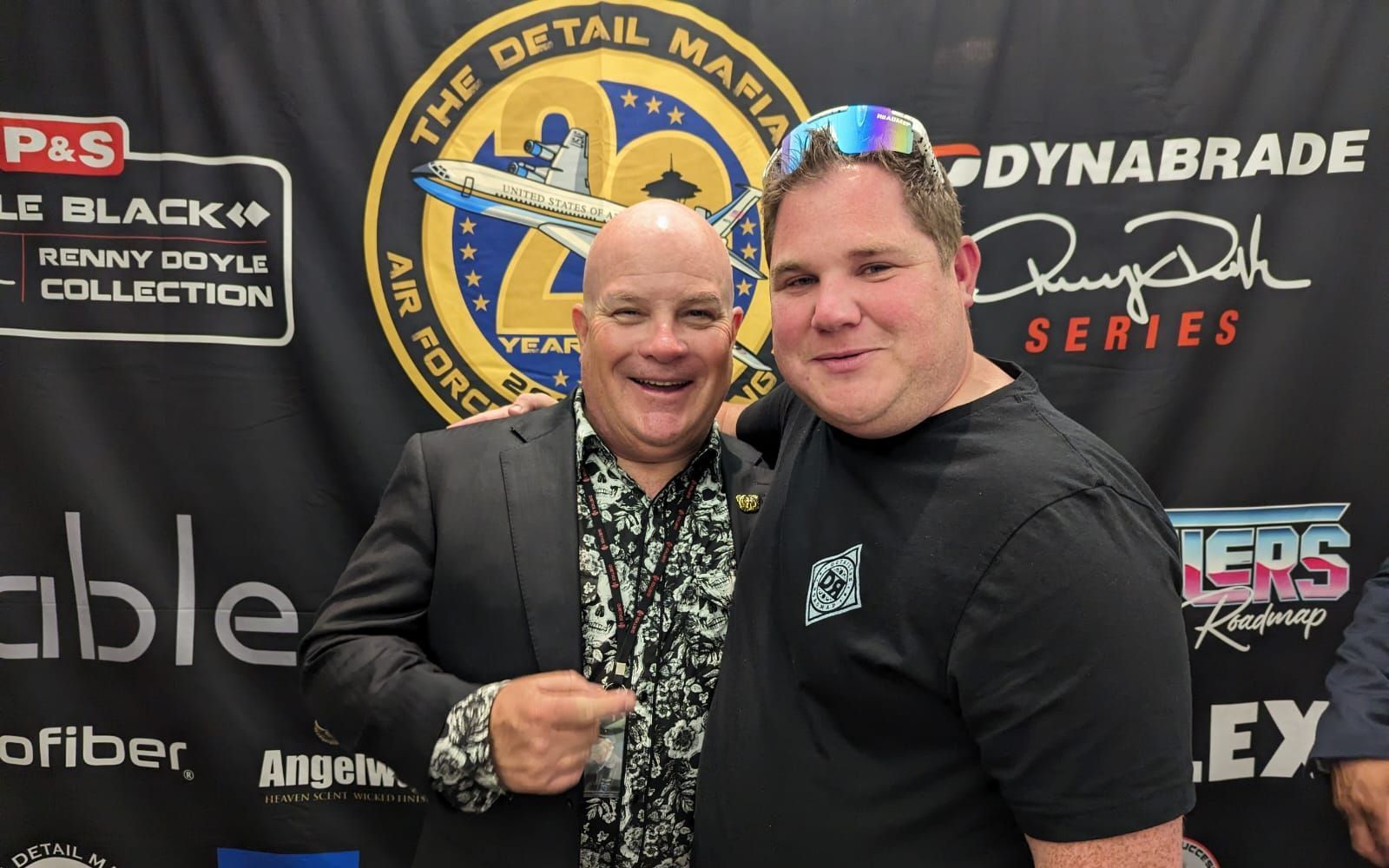 Two men are posing for a picture in front of a sign that says dynabrade series