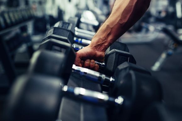 Hand gripping a dumbbell in a dimly lit gym with rows of weights in the background