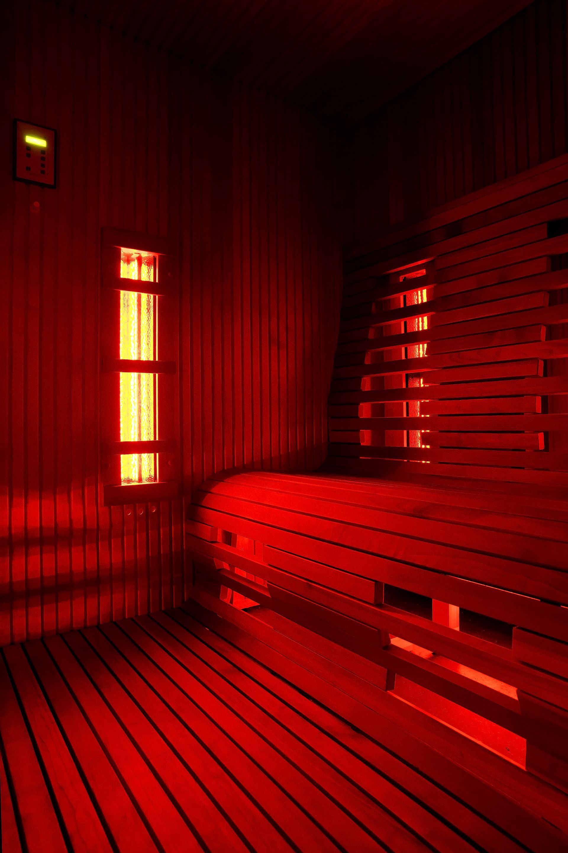Red-lit sauna interior with wooden benches and slatted walls