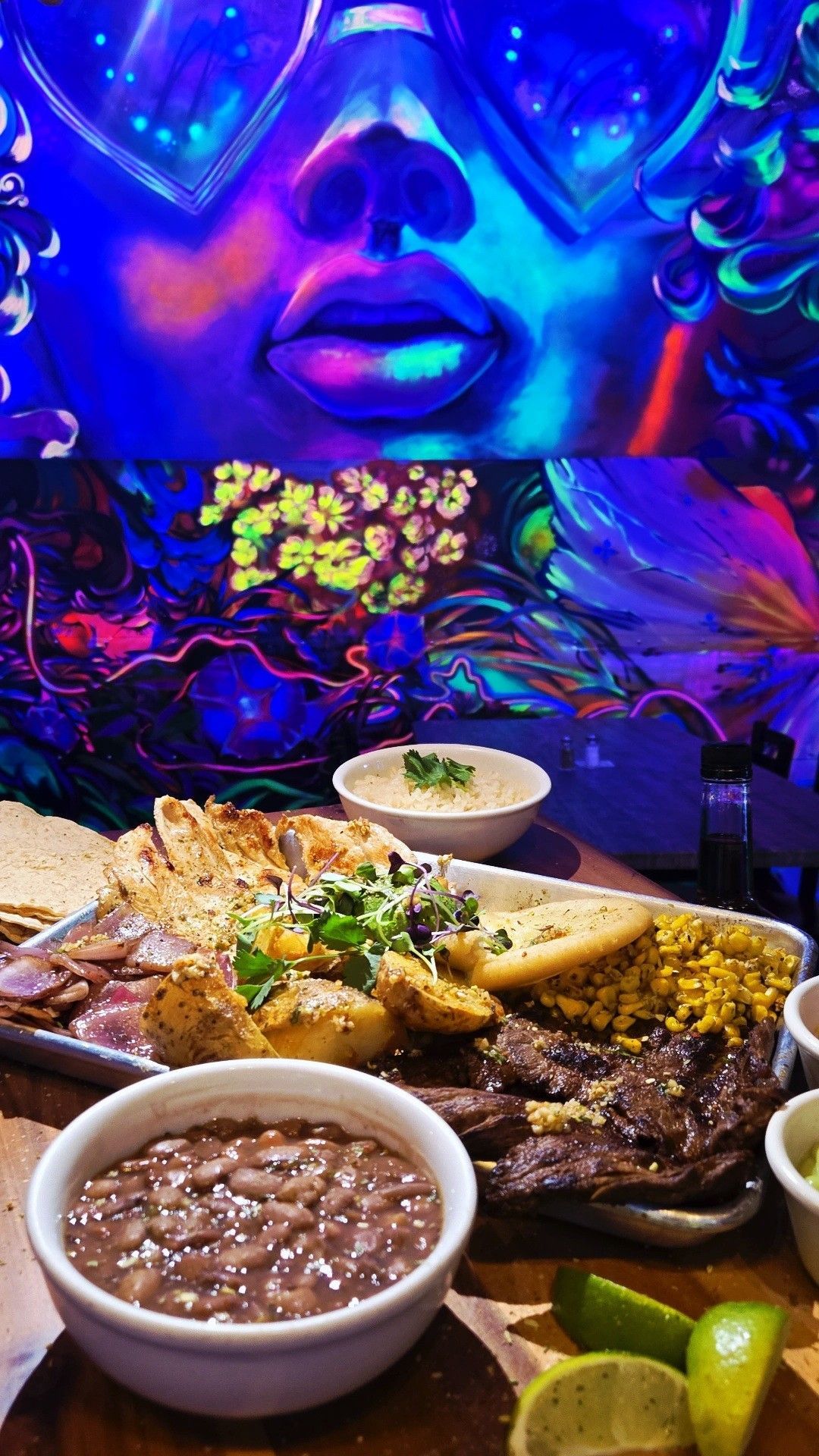 A colorful platter of food with sides in bowls. Illuminated woman's face and abstract shapes in background.