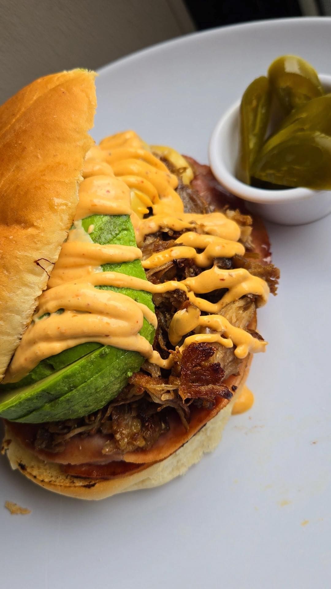 Sandwich with avocado and sauce on a plate with pickles.