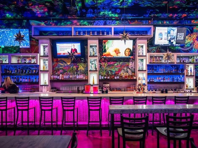 Brightly lit bar with pink underlighting, neon decor, and televisions.