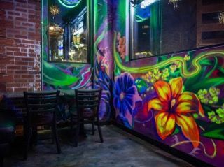 Two black chairs sit near a wall with vibrant floral murals. Brick wall on the left.