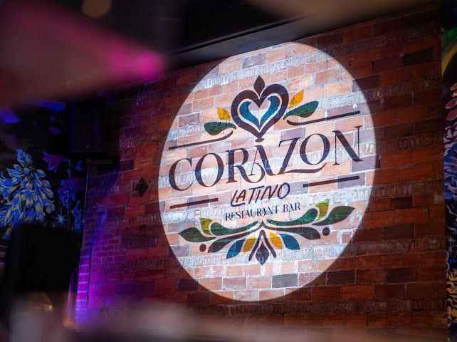 Corazon Latino sign projected on a brick wall with a decorative design and the words 