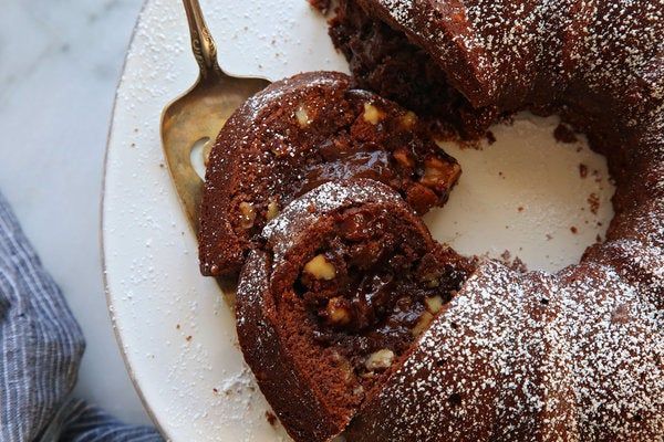 A chocolate bundt cake with a bite taken out of it is on a white plate.
