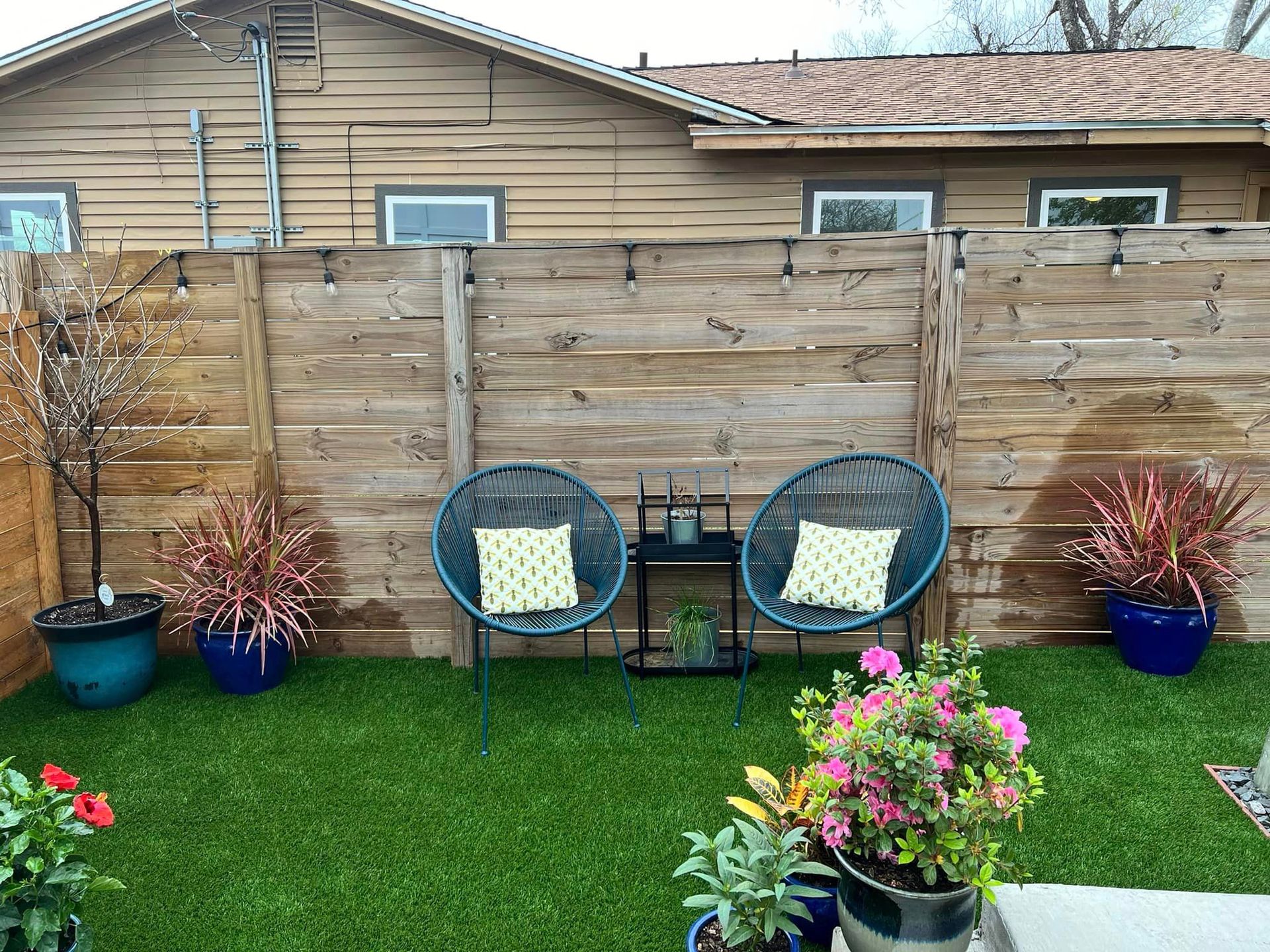 There are two chairs and a table in the backyard of a house.