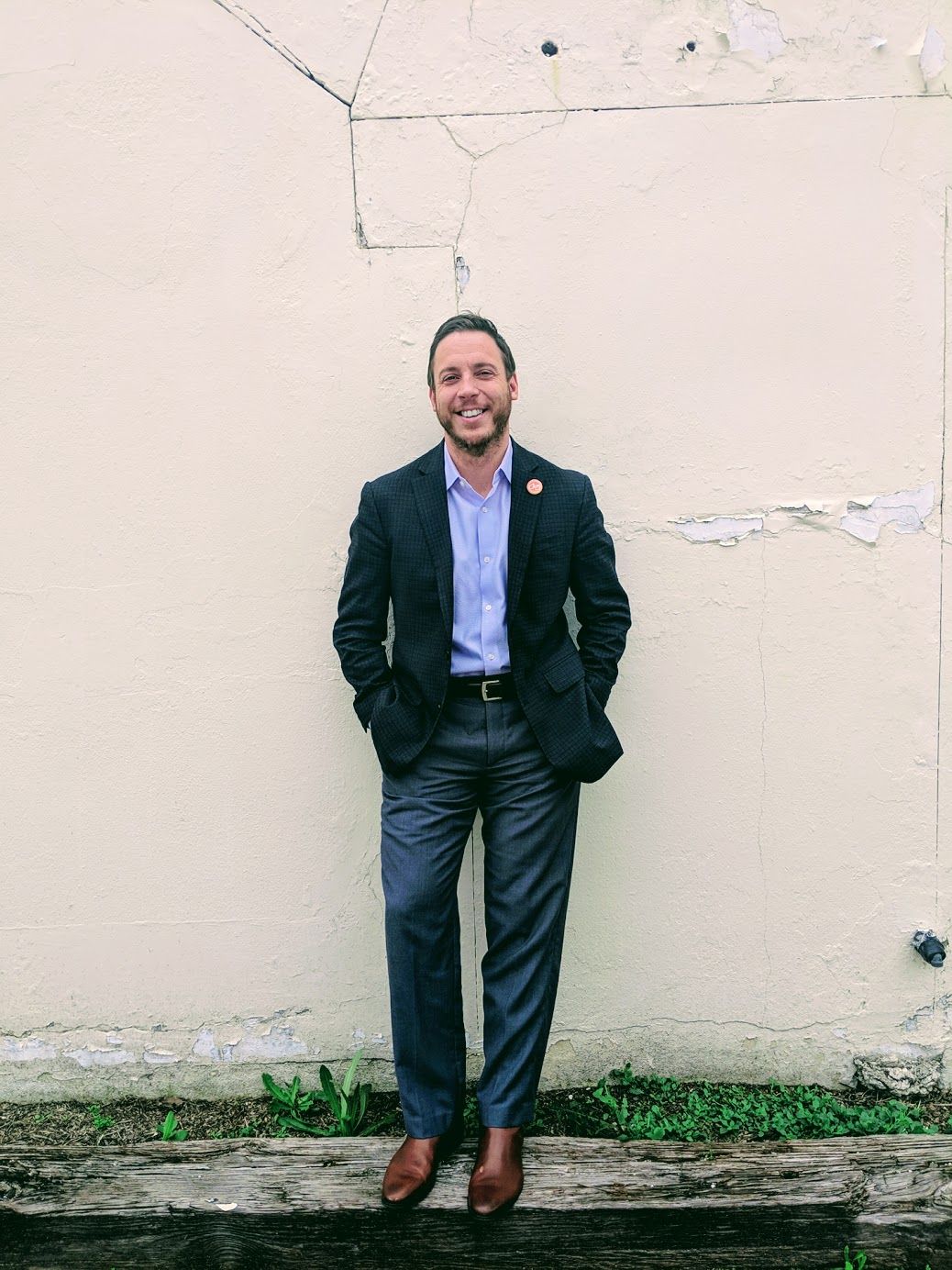 A man in a suit is standing in front of a white wall.