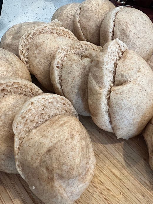 A bunch of rolls are sitting on top of a wooden cutting board.