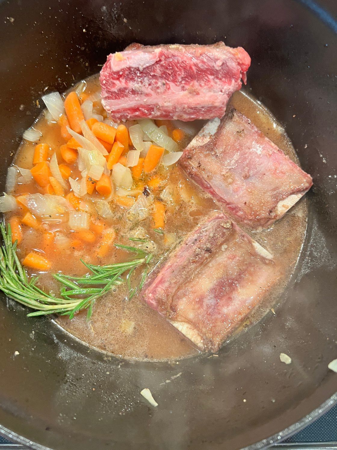 The ribs are being cooked in a pot with carrots and onions.