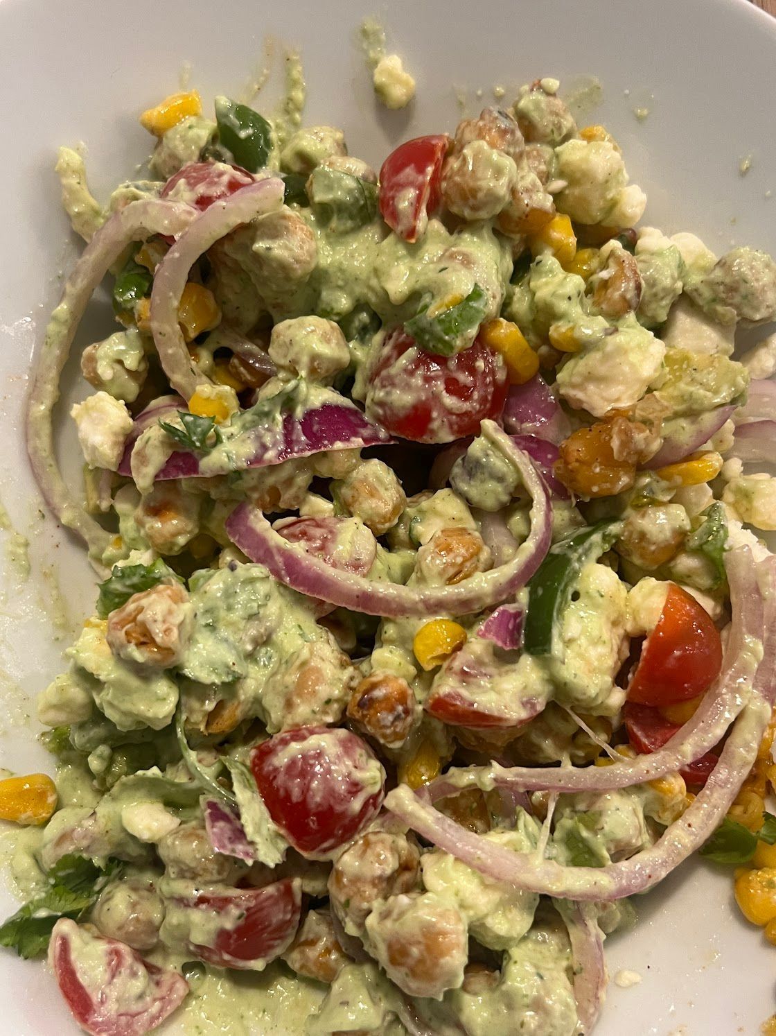 A close up of a salad with chickpeas , tomatoes , corn and onions on a plate.