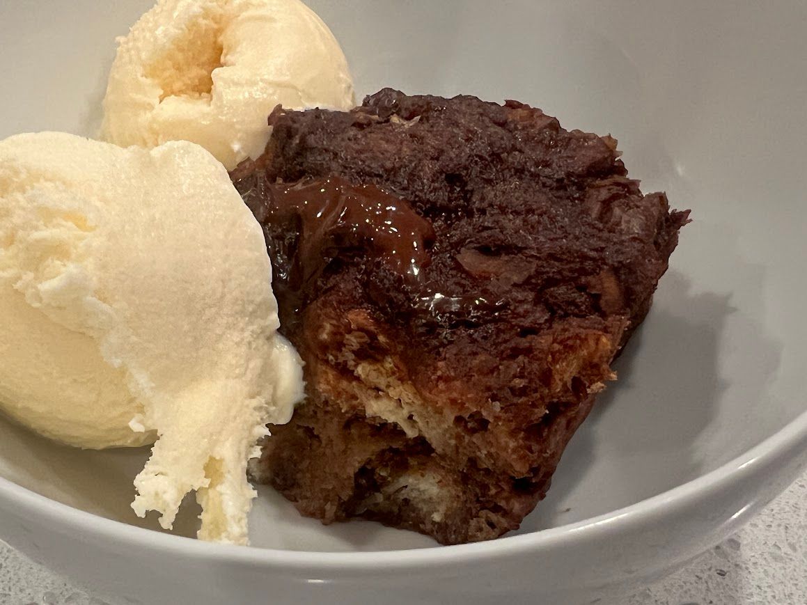 A white bowl filled with ice cream and a piece of chocolate bread pudding