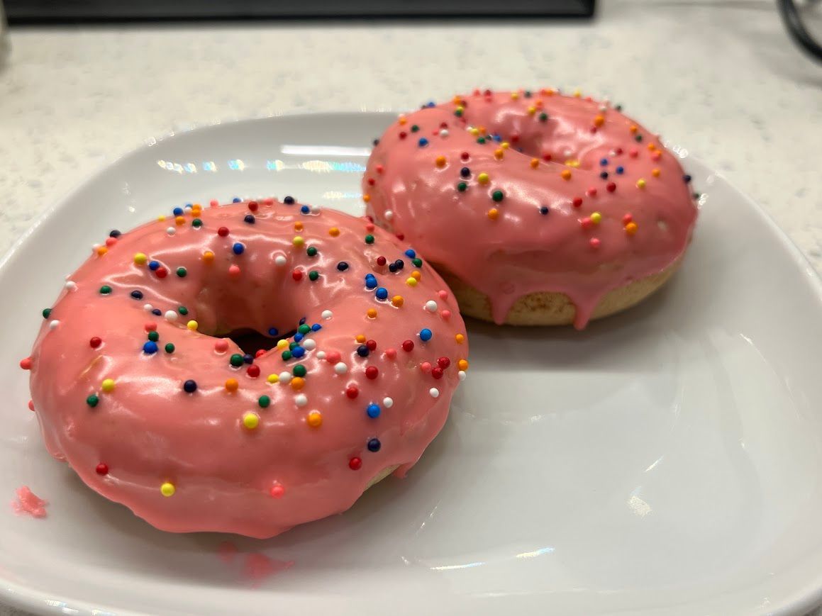 Two donuts with pink frosting and sprinkles on a white plate.