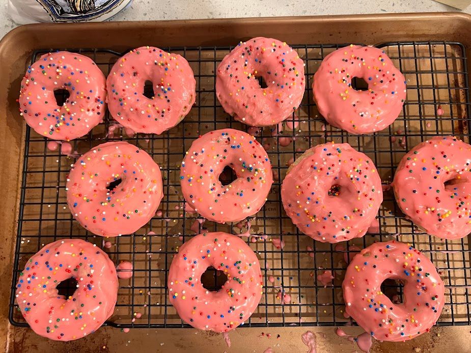 A tray of donuts with pink frosting and sprinkles on a cooling rack.