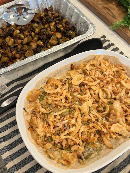 A casserole dish filled with fried onions is sitting on a table next to a pan of brussels sprouts.
