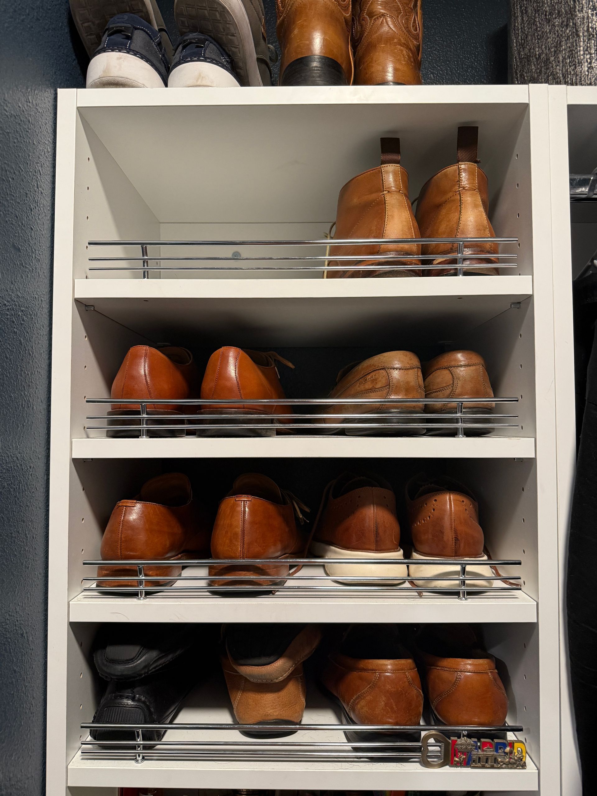A white shoe rack filled with brown shoes and boots.