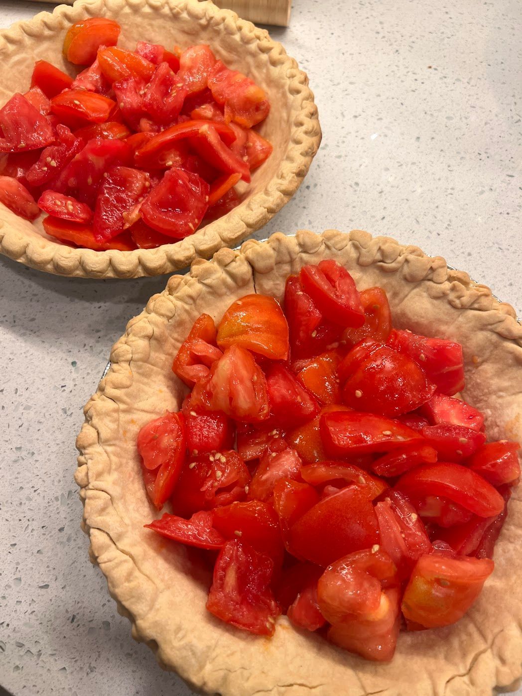 Two pie crusts filled with chopped tomatoes on a table.