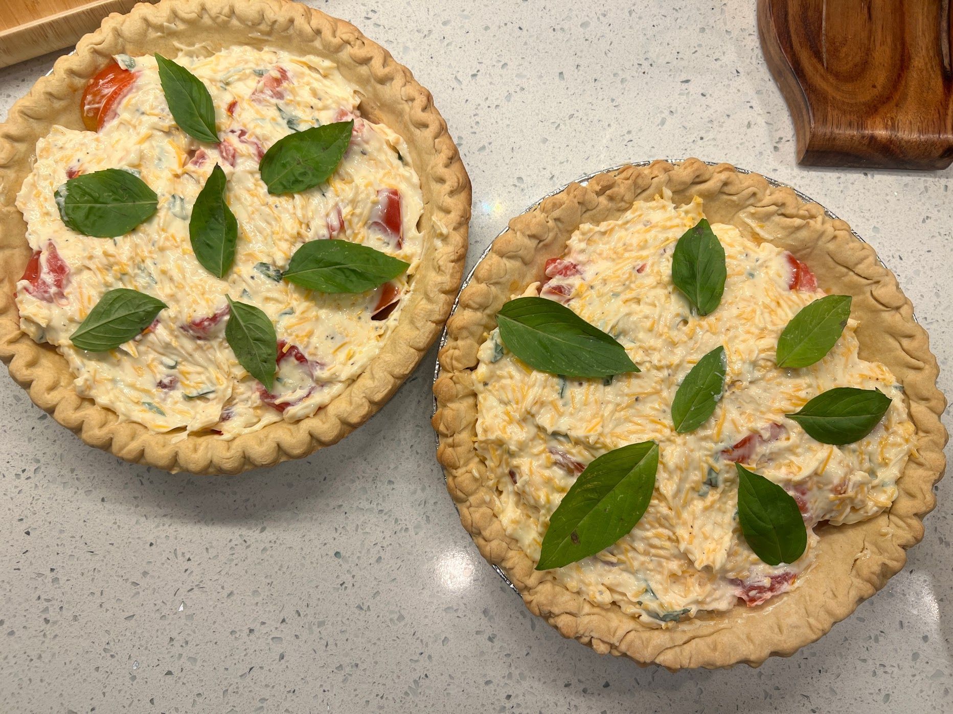 Two pies with tomatoes and basil on them are sitting on a counter.