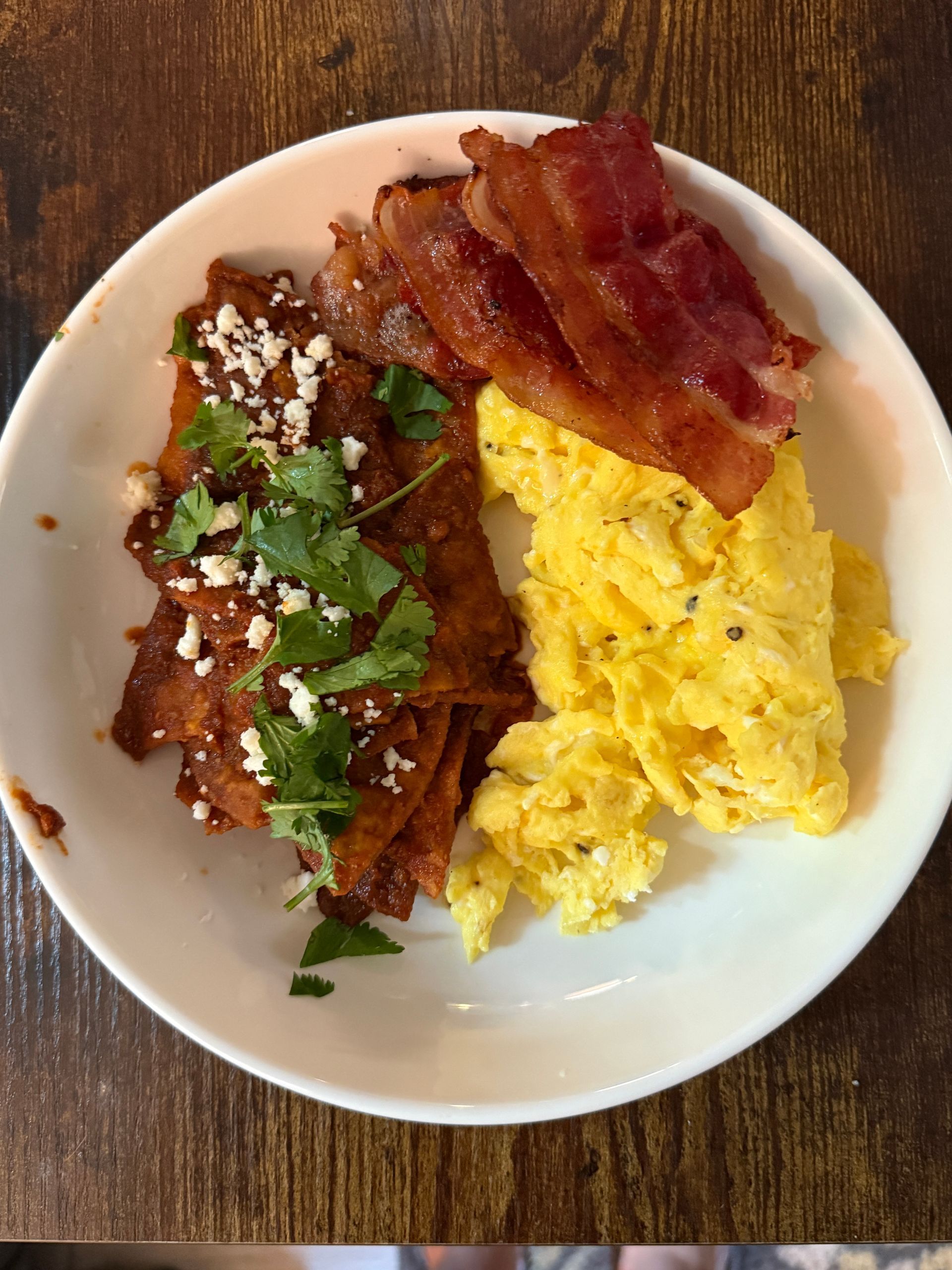 A plate of food with bacon and scrambled eggs on a wooden table