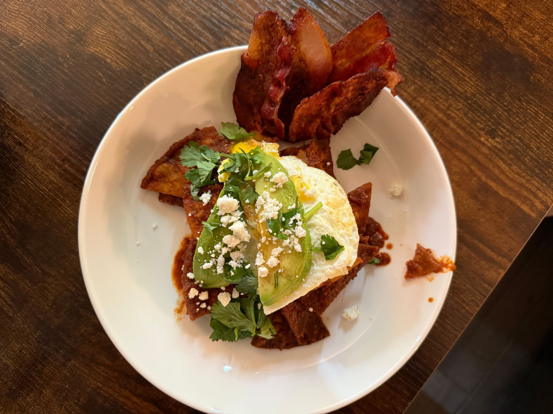 A white plate topped with eggs avocado and bacon on a wooden table.