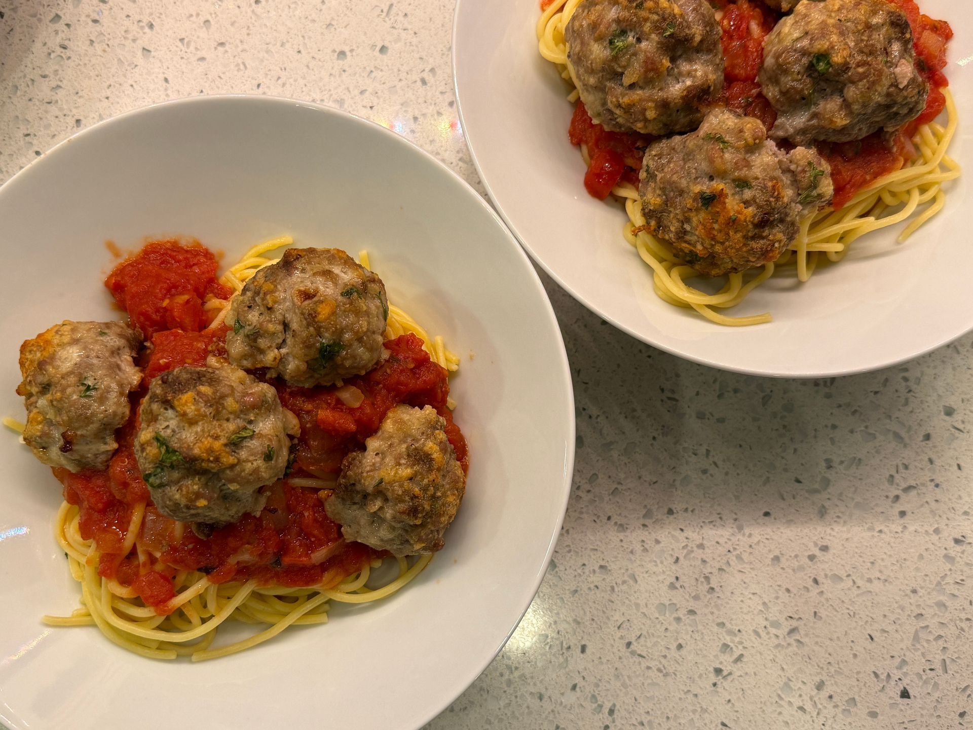 Two plates of spaghetti and meatballs with tomato sauce on a counter.