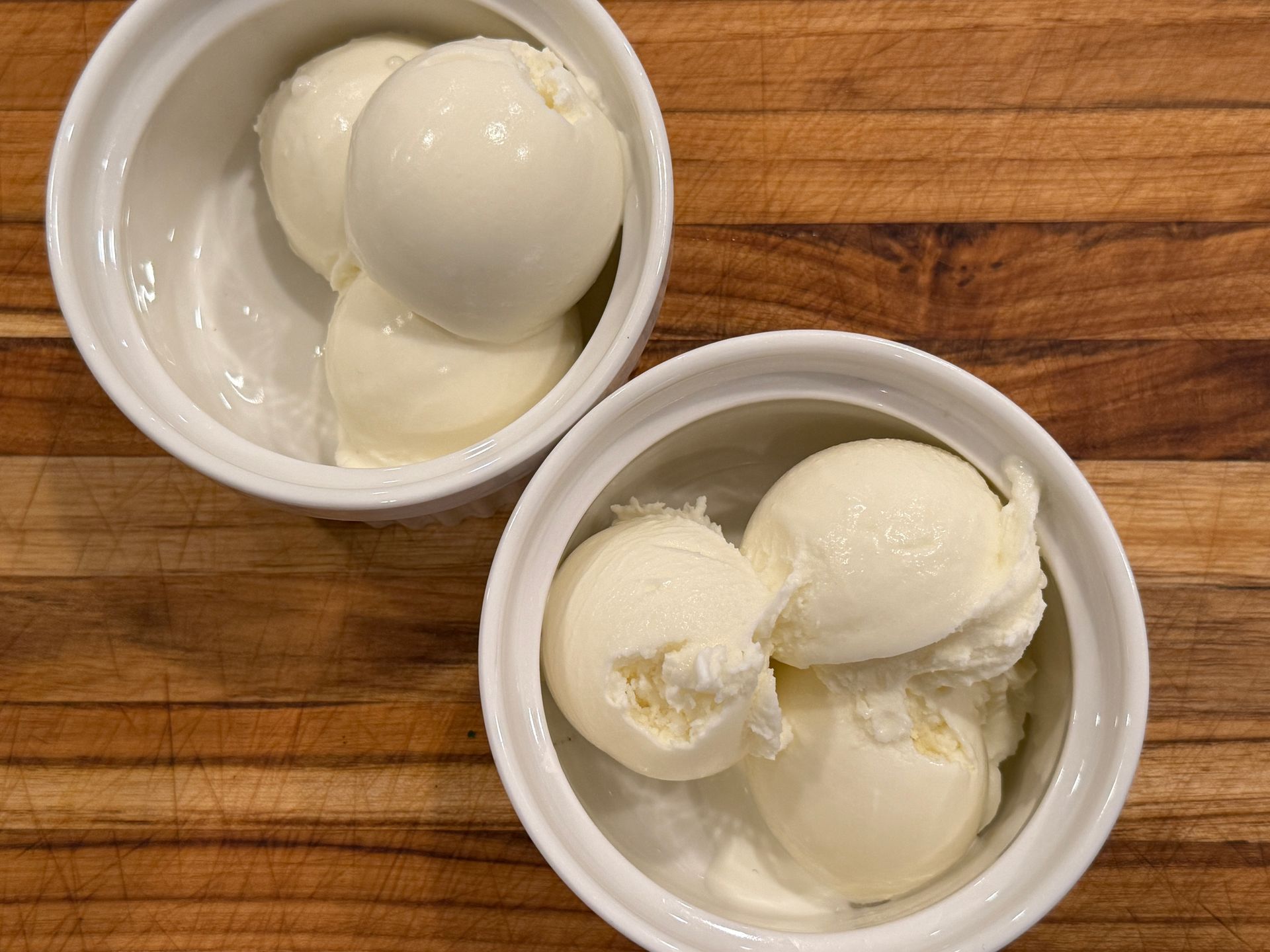 Two bowls of ice cream are on a wooden table.