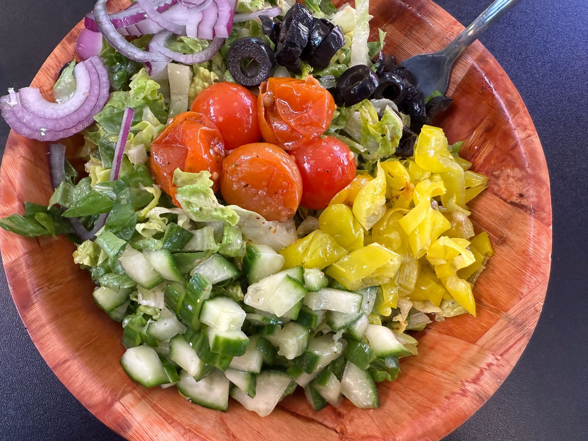 A salad in a wooden bowl with tomatoes , cucumbers , olives and onions.