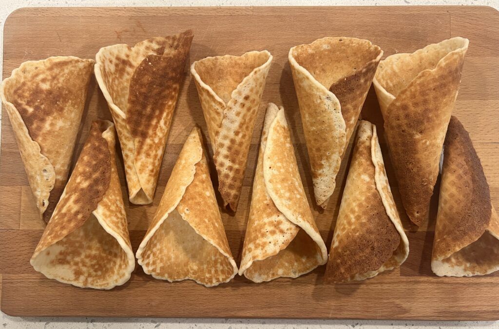 A wooden cutting board topped with a row of waffle cones.