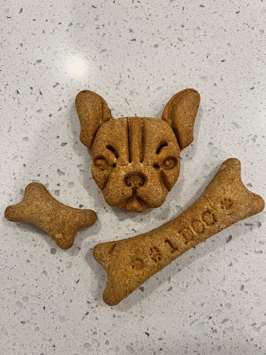 A french bulldog cookie , a dog bone , and a dog treat on a counter.