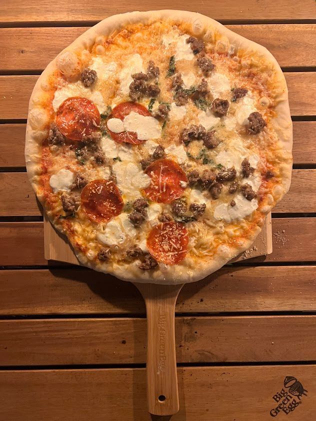 A pizza is sitting on a wooden paddle on a wooden table.