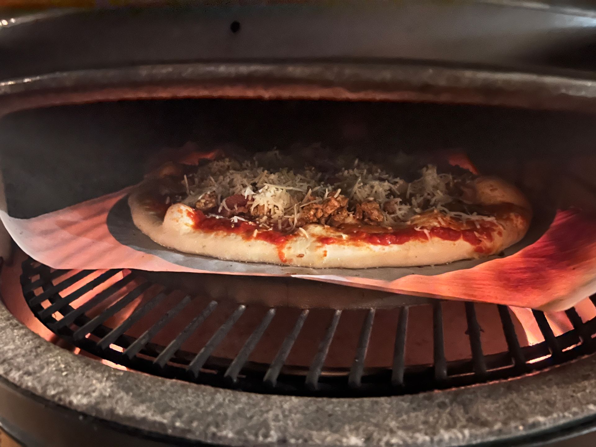 A pizza is cooking on a grill with a piece of wax paper on it