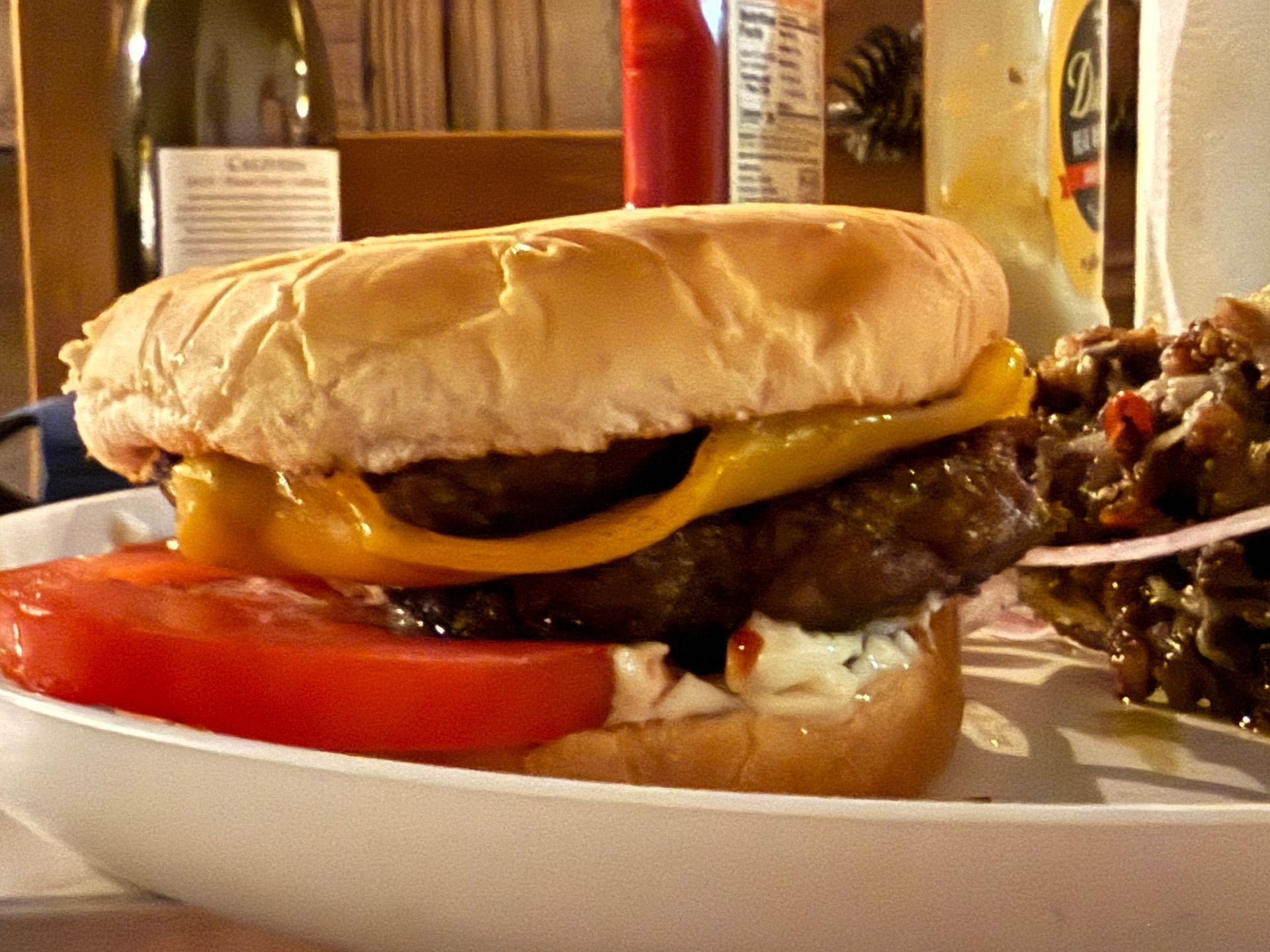 A close up of a hamburger on a plate with a fire pit in the background.