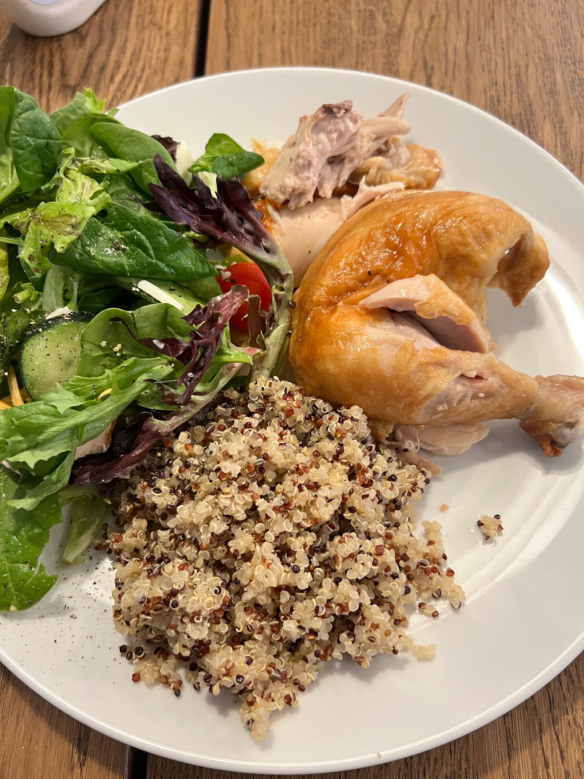 A white plate topped with chicken , rice , and a salad on a wooden table.