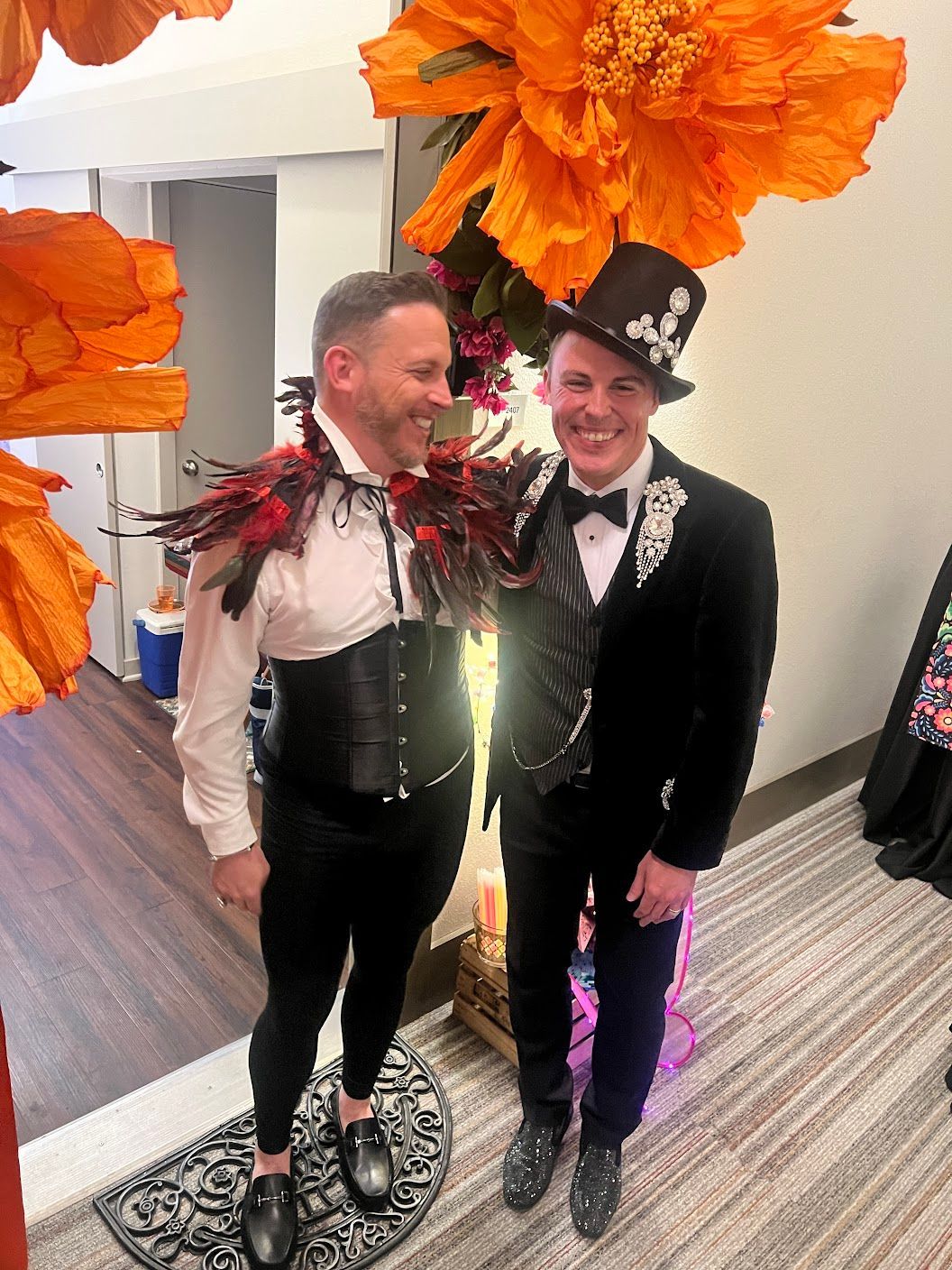 Two men are standing next to each other in a room with flowers hanging from the ceiling.