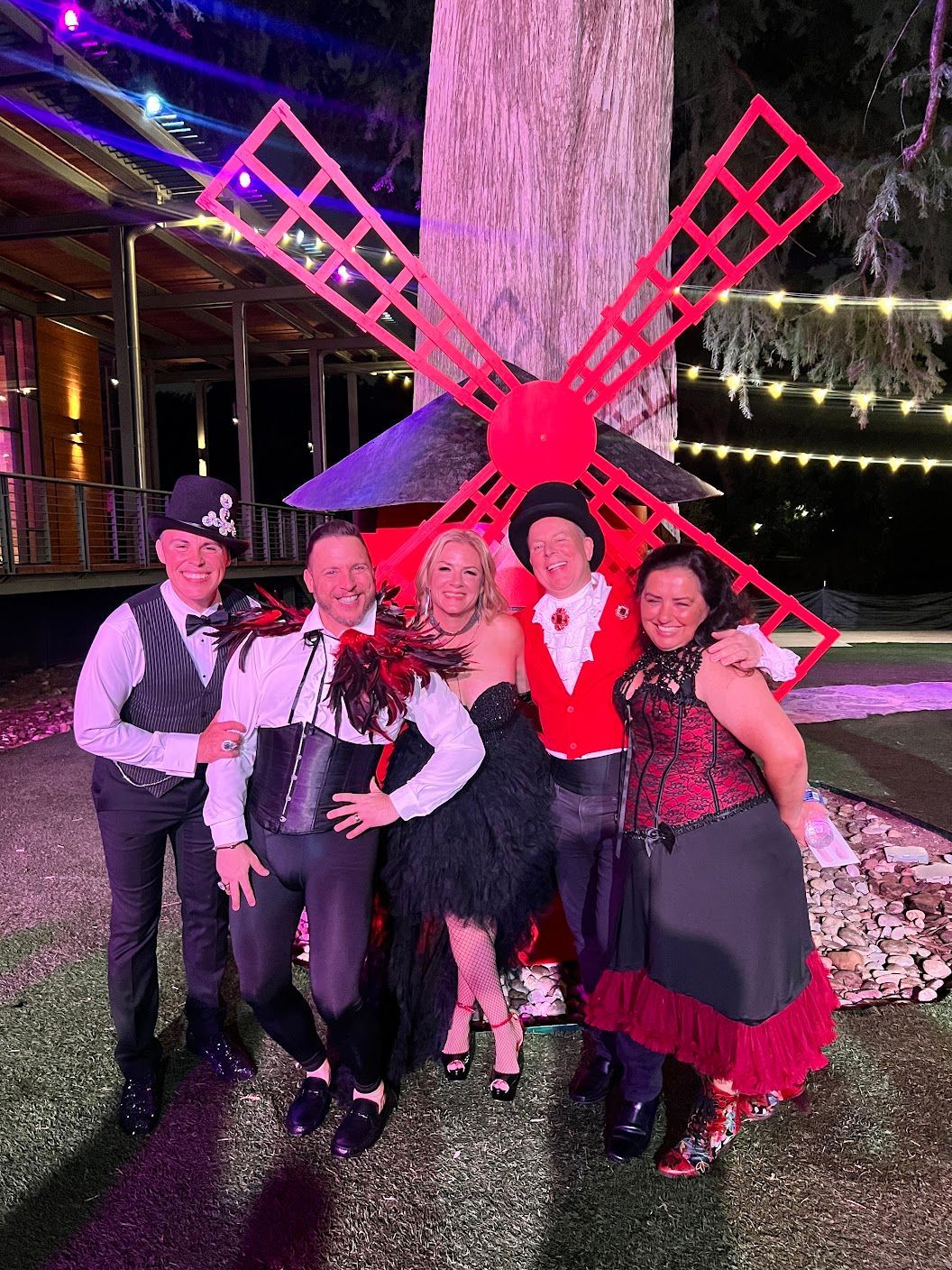 A group of people are posing for a picture in front of a red windmill.