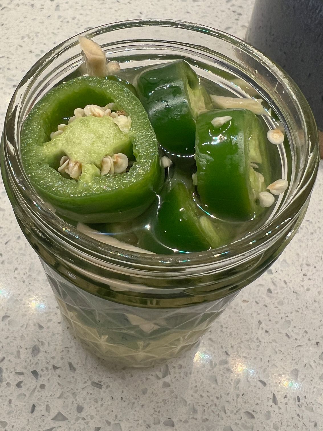 A jar filled with green jalapenos and water on a counter.