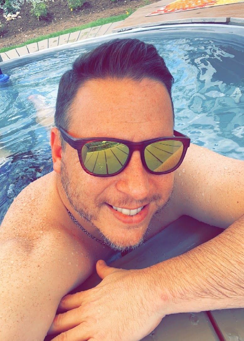 A man wearing sunglasses is laying in a hot tub.