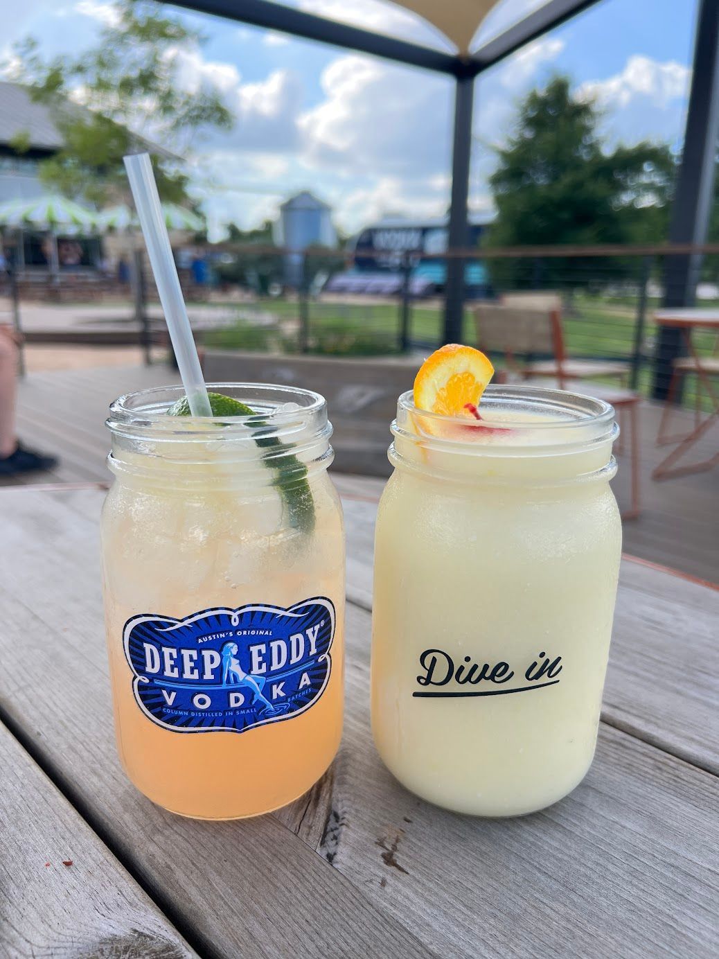 Two mason jars filled with drinks are sitting on a wooden table.