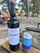 A bottle of wine and a can of beer are on a wooden table.