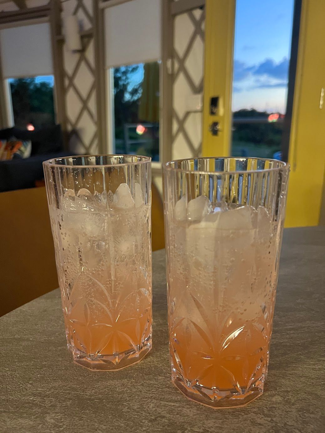 Two glasses filled with ice and a drink on a table.