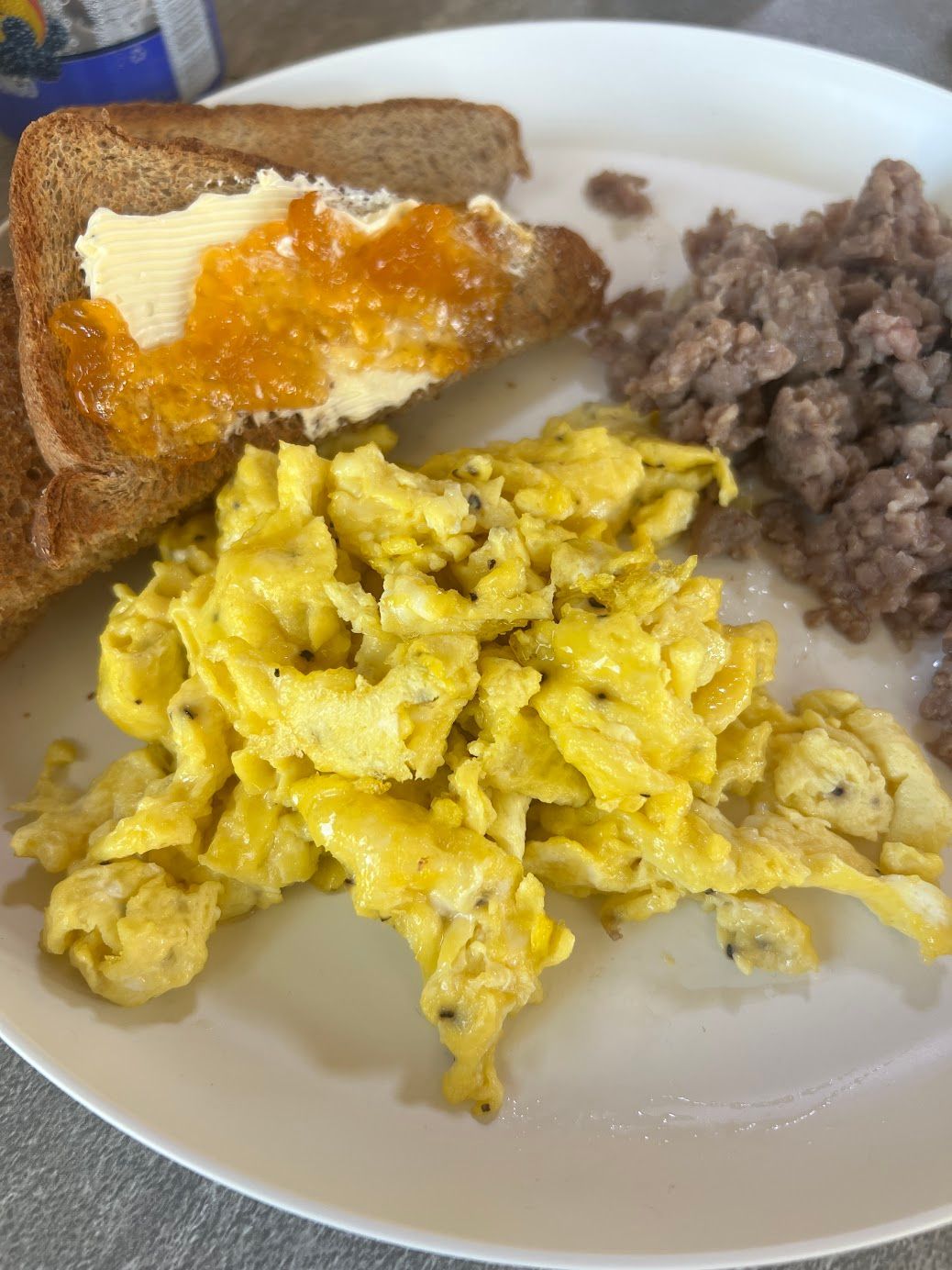 A white plate topped with scrambled eggs , toast , and meat.