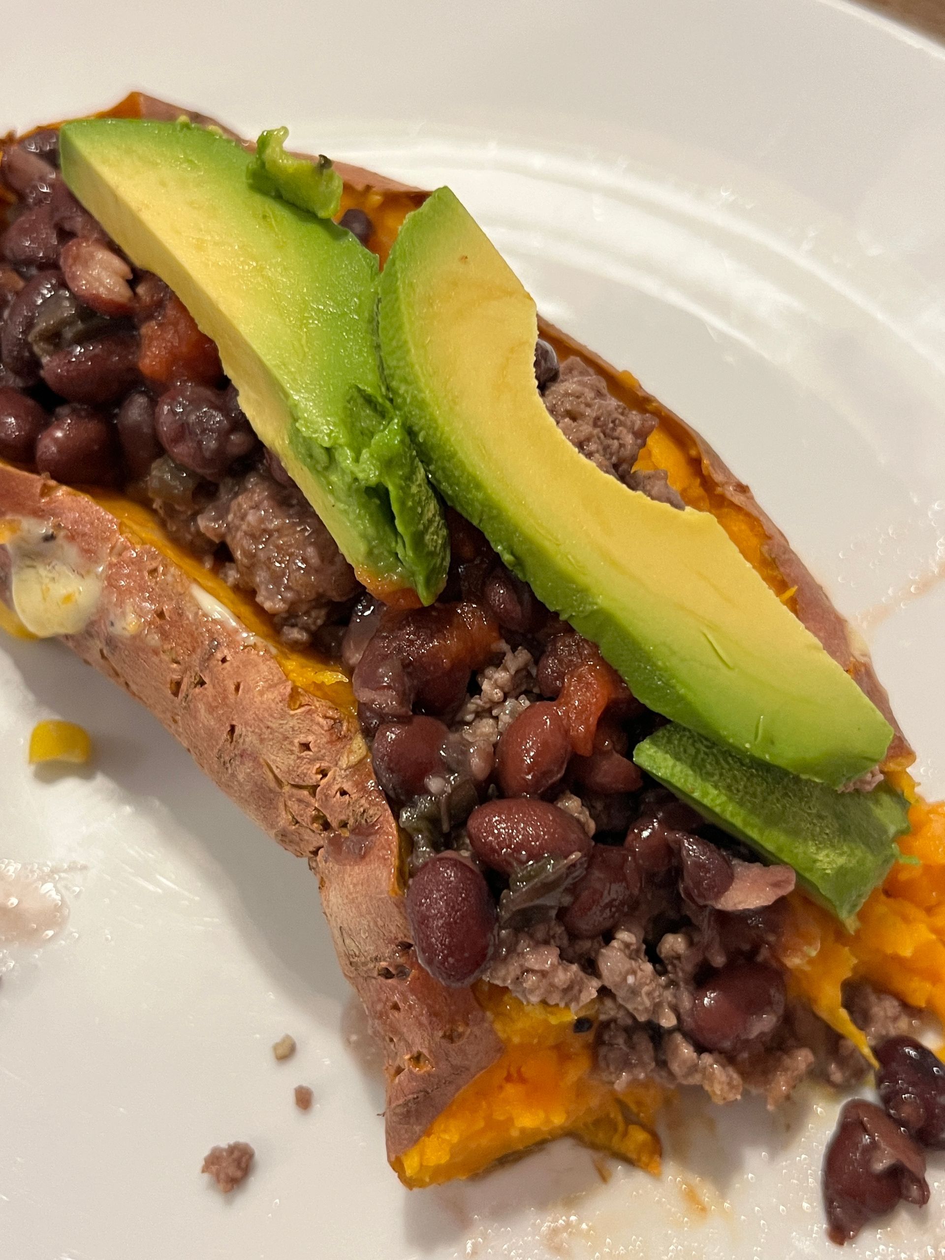 A close up of a sweet potato filled with beans and avocado on a plate.