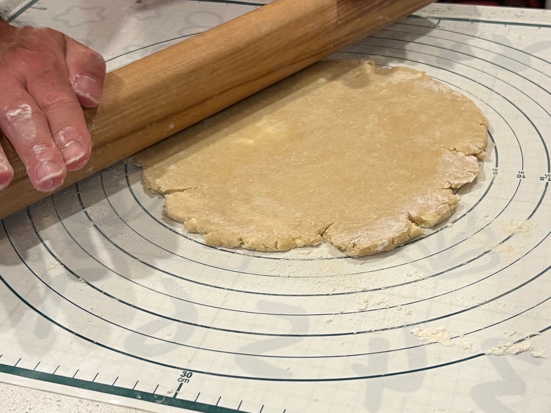 A person is rolling out a piece of dough on a silicone mat.