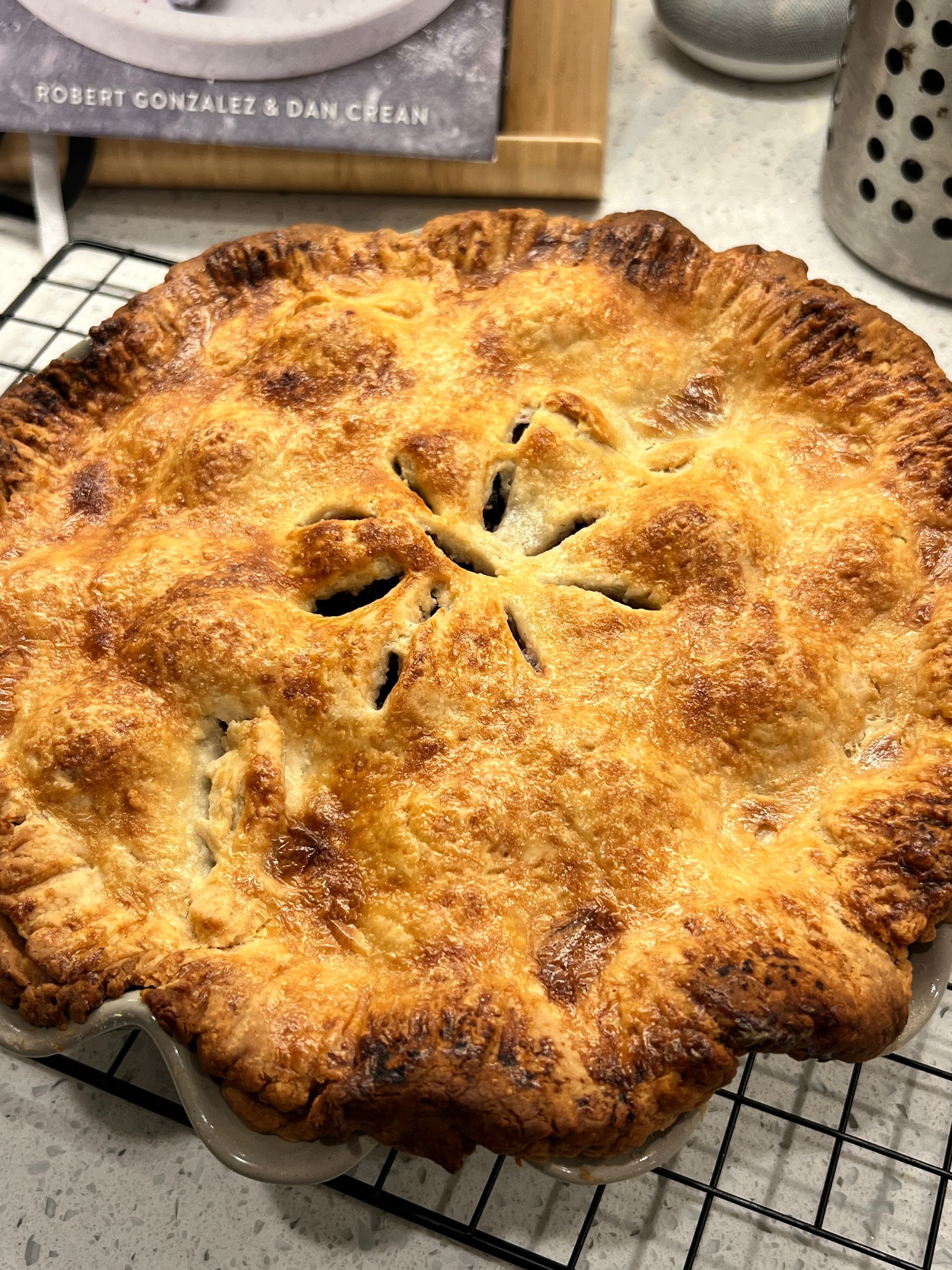 A pie is sitting on a cooling rack on a counter.