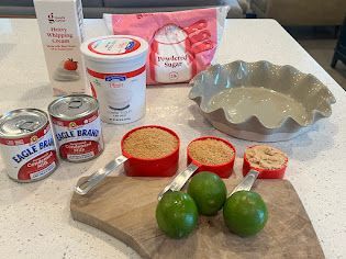A table topped with a cutting board , measuring cups , and limes.
