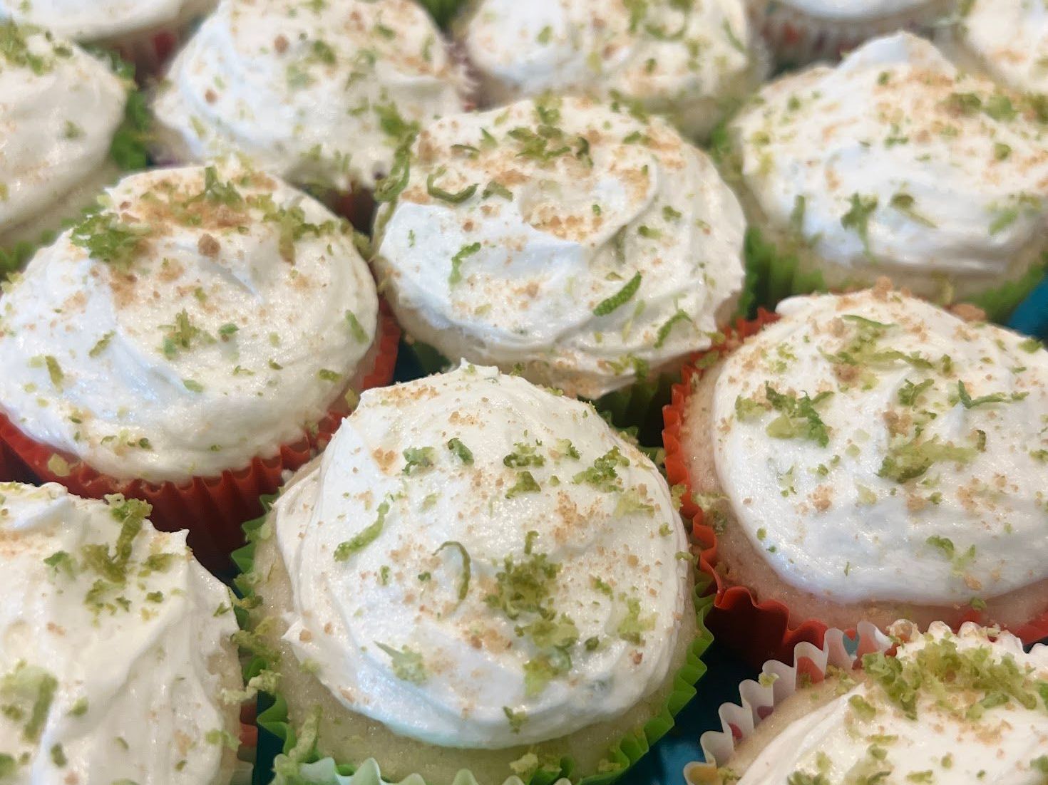 A bunch of cupcakes with white frosting and lime zest on top.