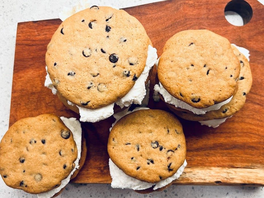 A wooden cutting board topped with chocolate chip cookies and whipped cream