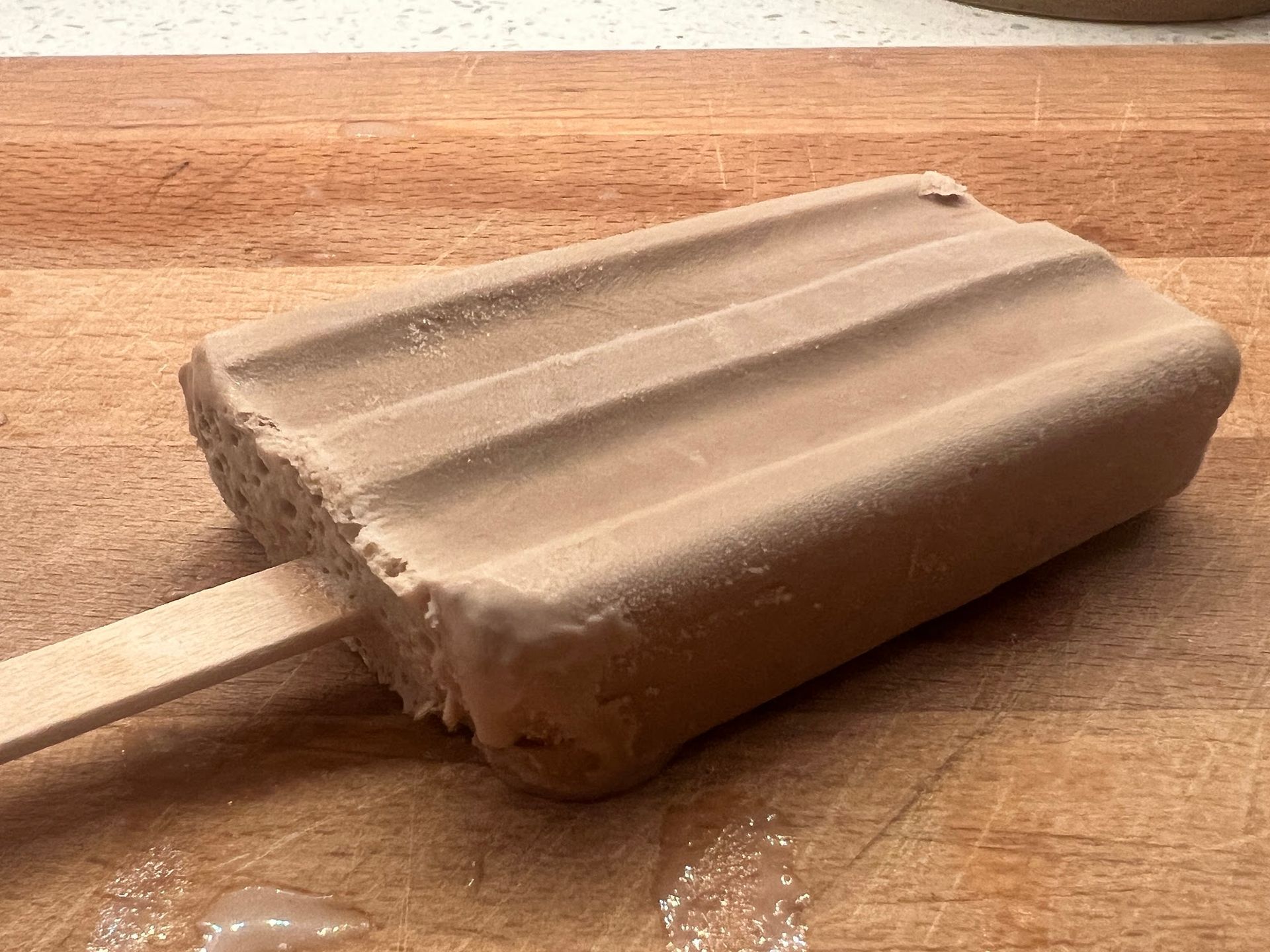 A chocolate popsicle is sitting on a wooden cutting board.